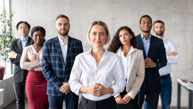 Successful International Management Professional Standing In Front Of Business Team Staff In Modern Office, Smiling To Camera. Leadership, Female Entrepreneurship And Career Growth Motivation Concept