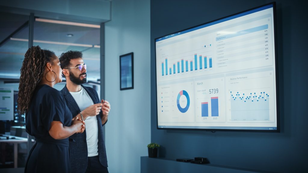 Company Operations Manager Holds Meeting Presentation. Black Female and Hispanic Male Uses TV Screen with Growth Analysis; Charts; Statistics and Data. People Work in Business Office.
